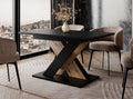 TOXX extending dining table with a black tabletop and wotan oak effect X-shaped base placed in a modern dining room setting, upholstered dining chairs arranged around the table on a rug.
