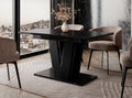 Extending dining table Muss with a black marble effect finish placed in a modern dining room setting, black pedestal base, upholstered dining chairs positioned around the table on a decorative rug.