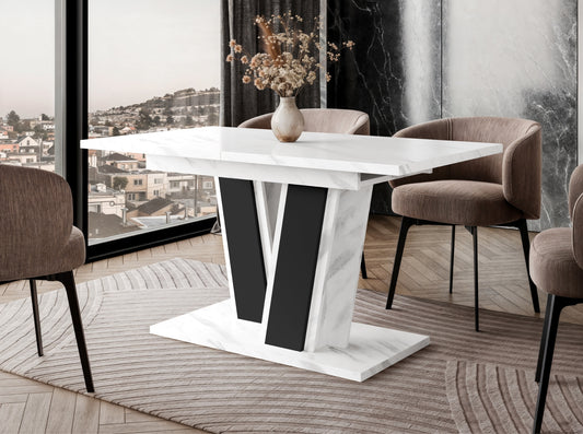 Extending dining table Muss styled in a modern dining room setting, white tabletop, black geometric pedestal base, placed on a rug next to upholstered dining chairs and a large window.